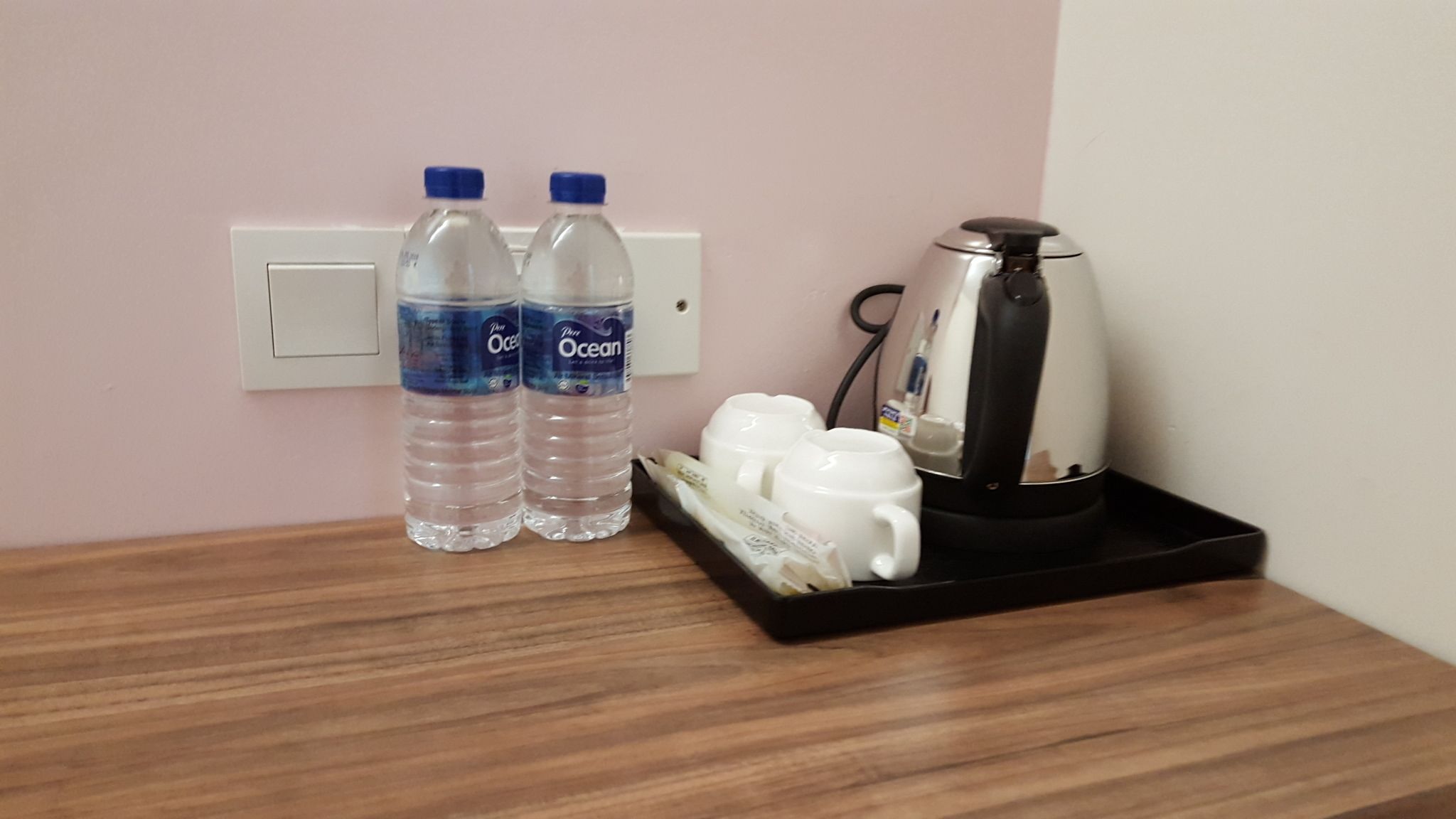 A wooden table with two water bottles, a coffee maker, and a tray with cups.