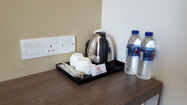 A hotel room with a wooden nightstand, a kettle, two water bottles, a tray with cups, and a no-smoking sign. - River View Inn Nusa Bestari Skudai (Johor Bahru)
