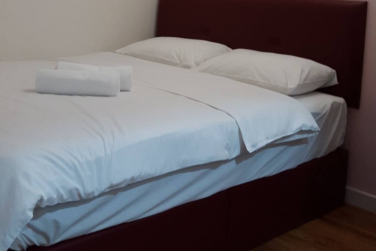 Un lit simple avec une tête de lit en bois, dans une pièce aux murs blancs et roses.
