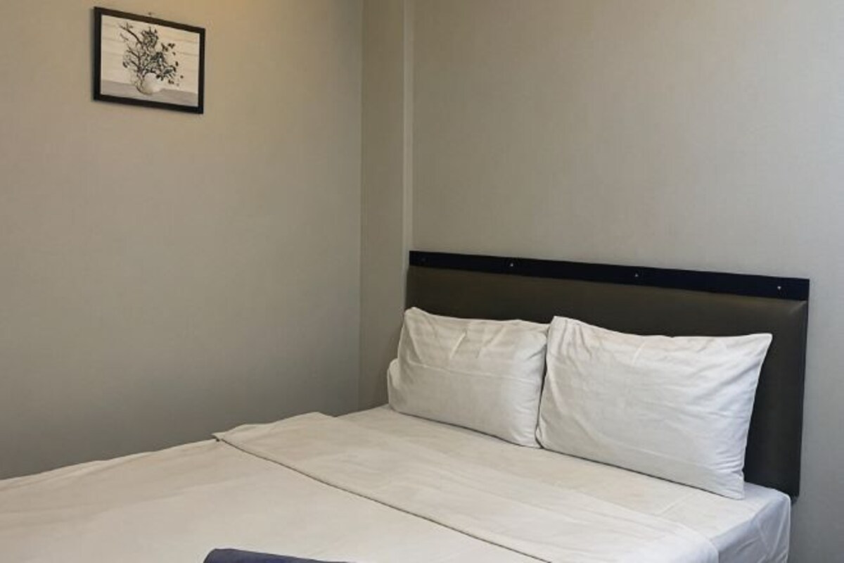 Una cama bien hecha con un cabecero oscuro y ropa de cama blanca en una habitación sencilla.