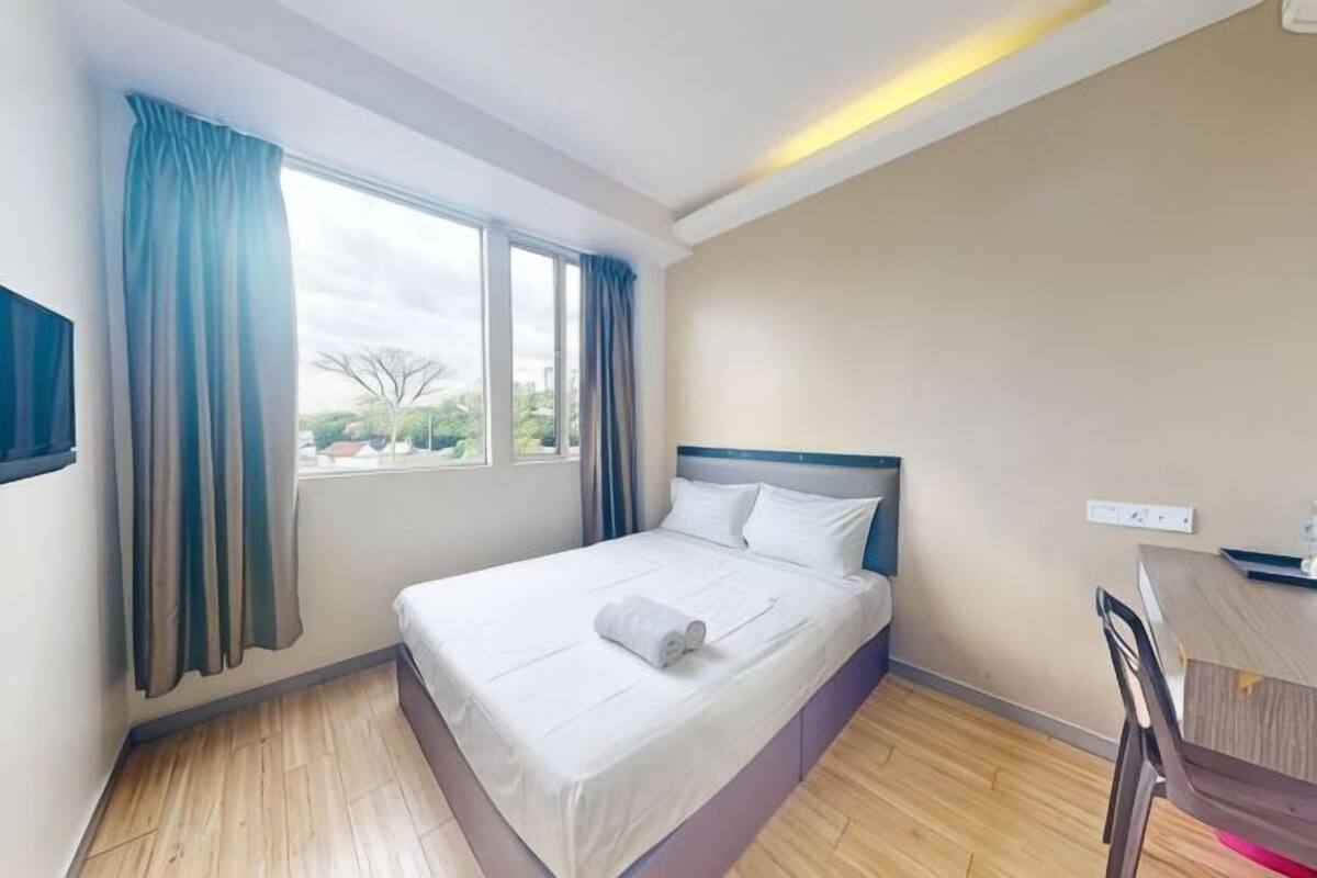Une chambre d’hôtel avec un lit, un bureau, une chaise, une fenêtre avec des rideaux et une vue sur l’extérieur.