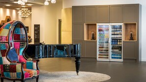 A modern lobby with a black piano, colorful armchair, and two beverage refrigerators. - elaya hotel leipzig city center (Leipzig)
