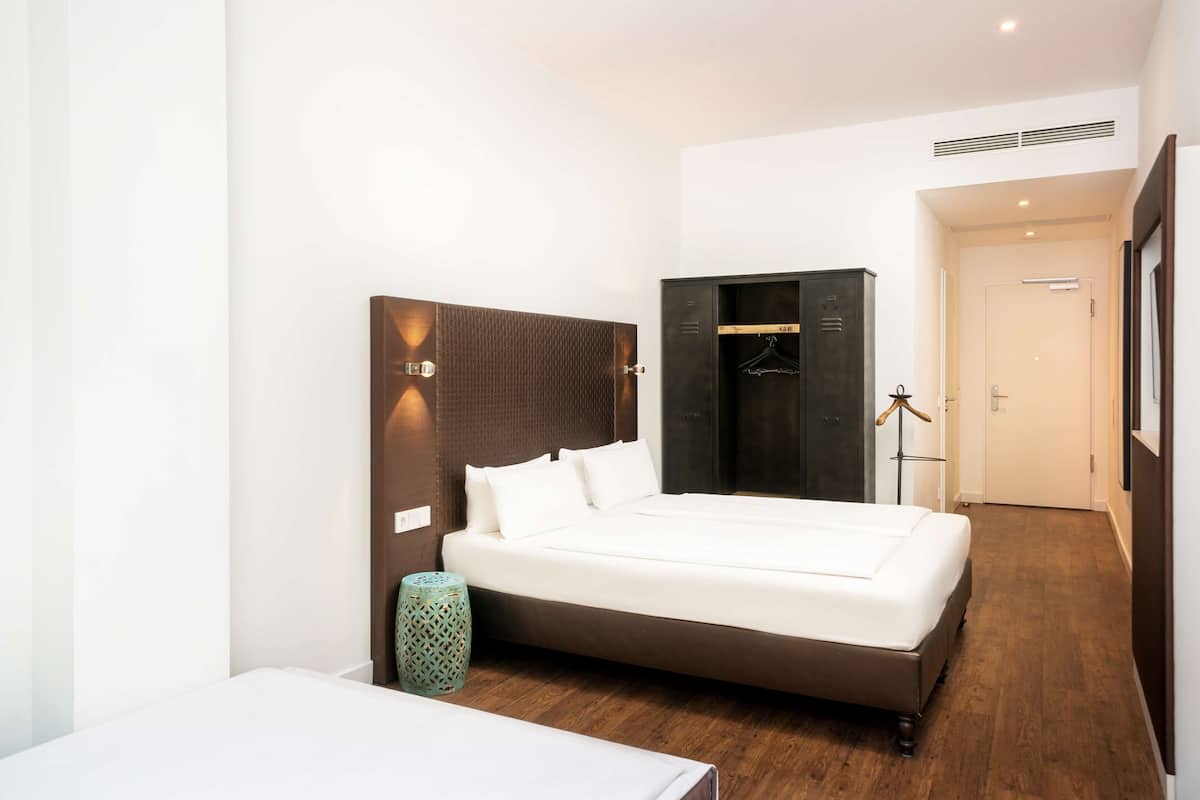 A modern hotel room with a large bed, a wardrobe, a bedside table, and a lamp.