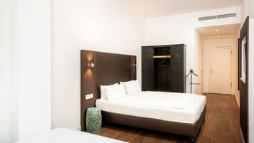 Ein modernes Hotelzimmer mit einem großen Bett, einem Kleiderschrank, einem Nachttisch und einer Lampe.