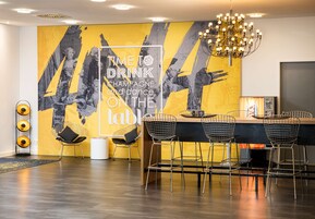 Een moderne barruimte met een grote muurschildering, barstoelen en een kroonluchter.