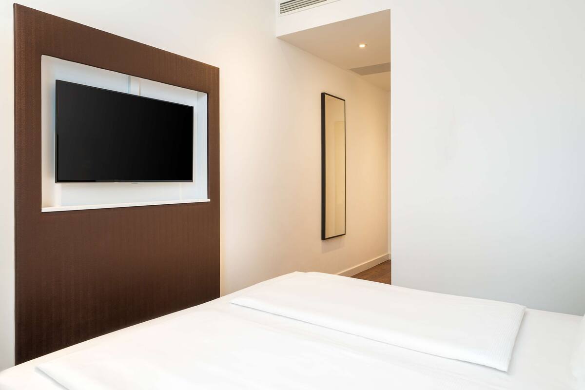 A hotel room with a bed, a mounted television, and a mirror.