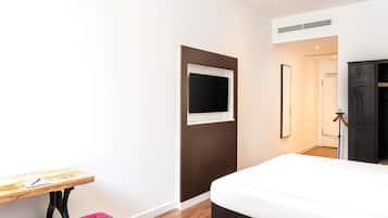 A hotel room with a bed, a desk, a TV mounted on the wall, and a wardrobe.