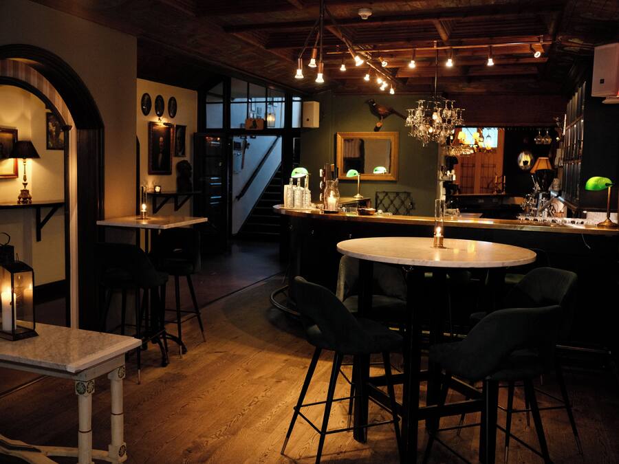 A bar area with a round table, bar stools, and a chandelier.