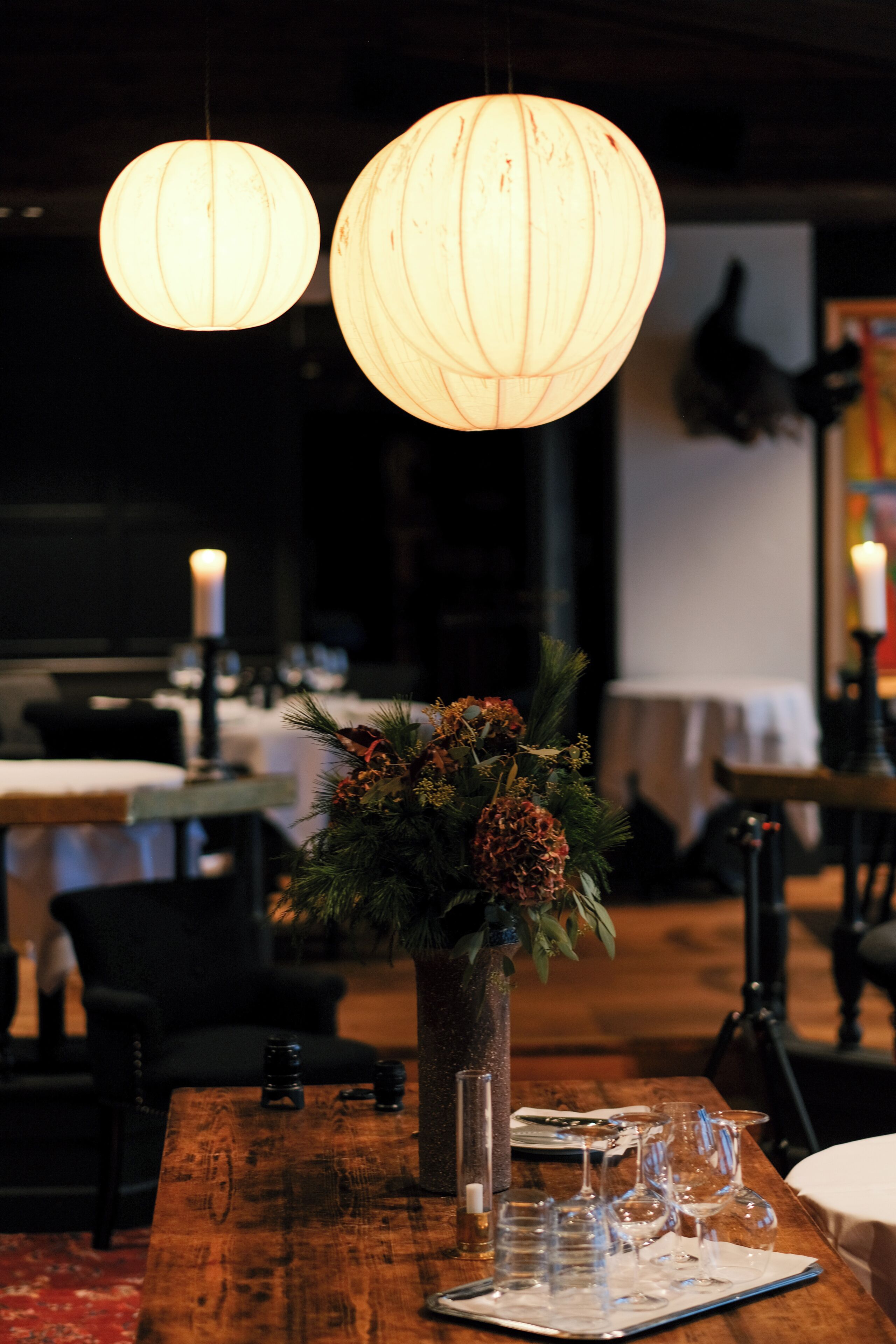 Una mesa de comedor con un florero, lámparas colgantes y una vela.
