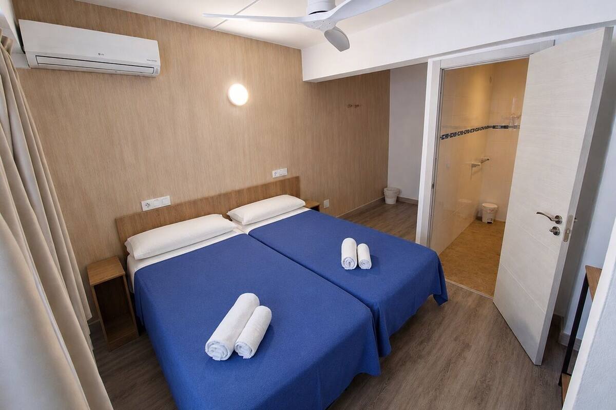 A hotel room with two beds, an air conditioning unit, a ceiling fan, and a bathroom visible through an open door.