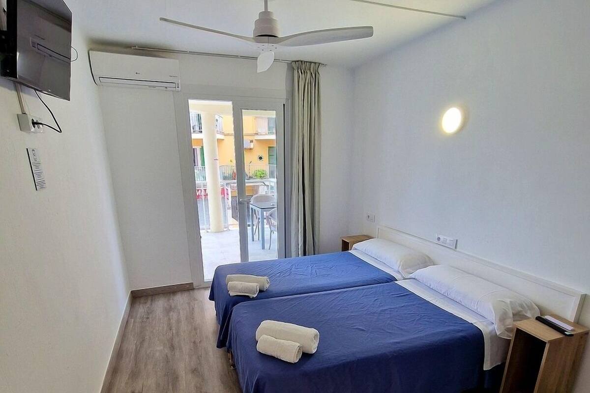 A hotel room with two beds, a ceiling fan, a TV mounted on the wall, and a balcony with a view.