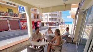 An outdoor seating area with a table and chairs, a view of the street, and a building with a sign. - Hostal Sol de Mallorca. (Palma de Mallorca)