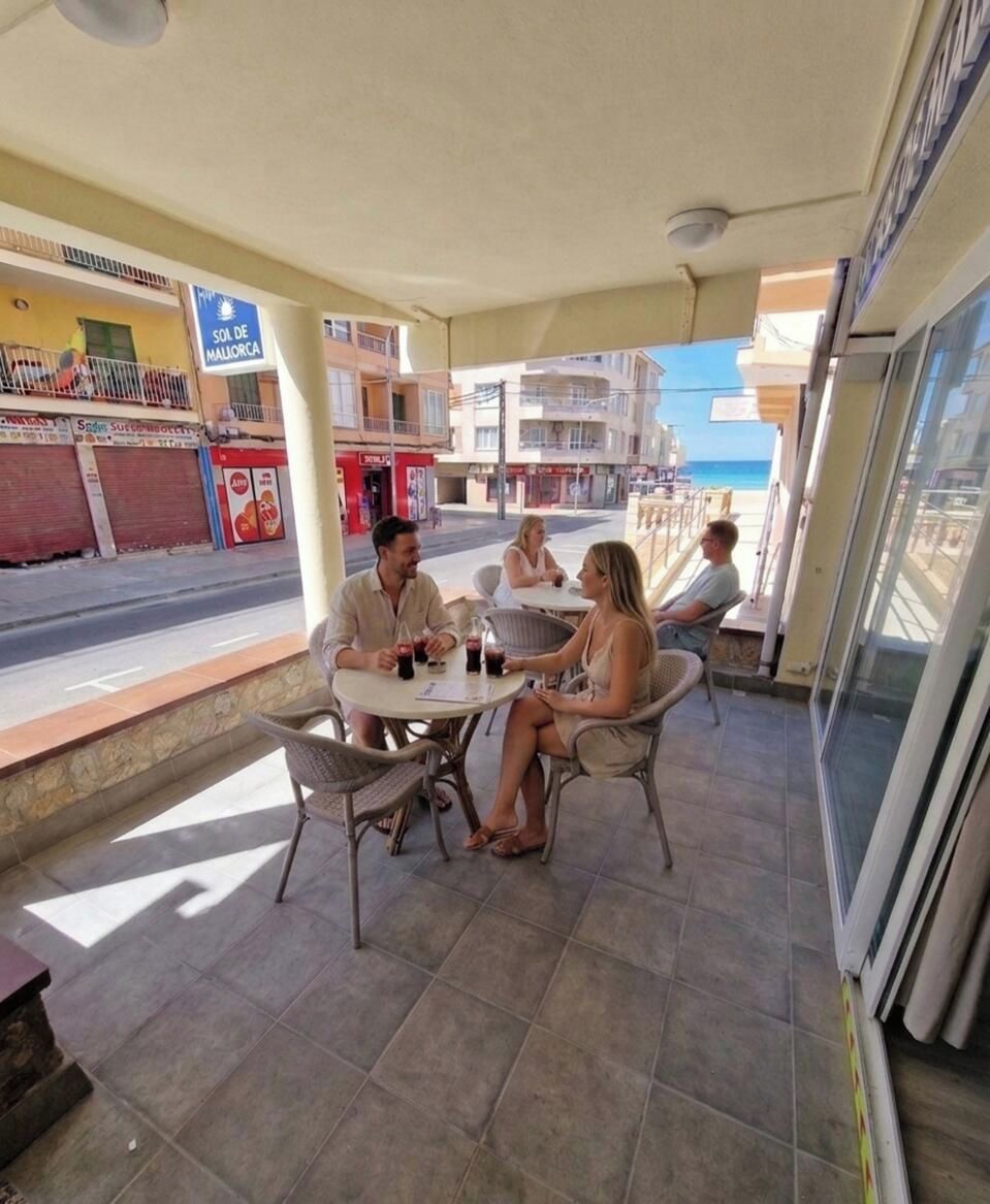 Un área de estar al aire libre con mesa y sillas, vista a la calle y un edificio con un letrero.