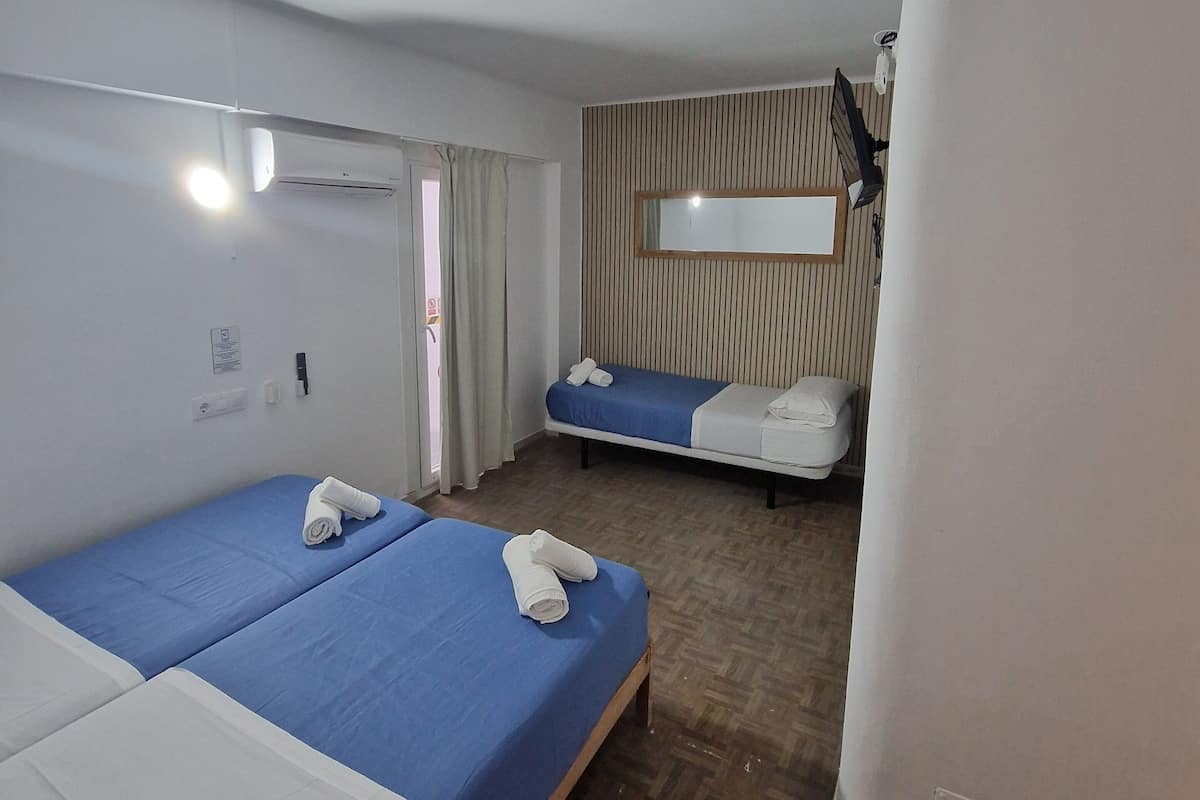 A hotel room with two beds, a wooden floor, a ceiling fan, and a window with curtains.