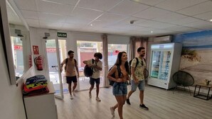 A hotel lobby with a 'SALIDA' sign, a fire extinguisher, a refrigerator, and a beach mural. - Hostal Sol de Mallorca. (Palma de Mallorca)