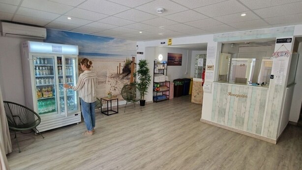 A spacious room with a wooden floor, a reception desk, a refrigerator, and a wall mural. - Hostal Sol de Mallorca. (Palma de Mallorca)