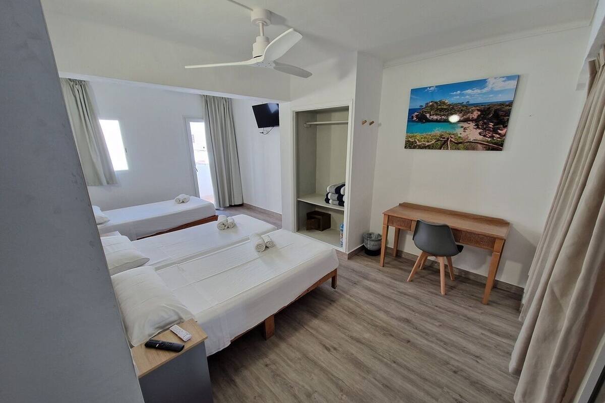 A hotel room with two beds, a desk, a chair, a TV, a painting, and a ceiling fan.