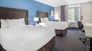 A hotel room with two beds, a desk, a chair, a lamp, and a window with curtains. - Days Inn and Suites by Wyndham Oxford (Oxford)