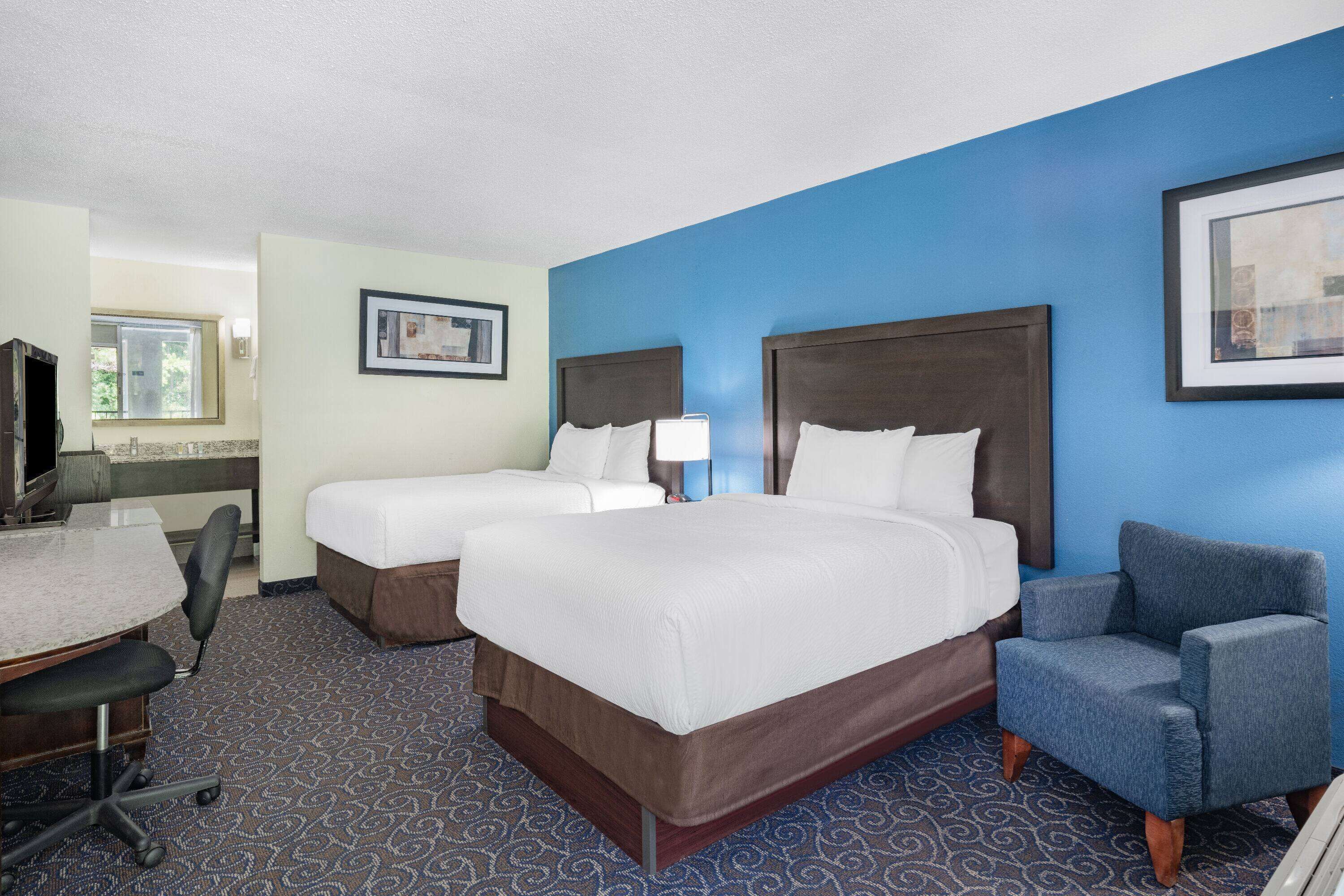 A hotel room with two beds, a desk, a chair, and a TV.