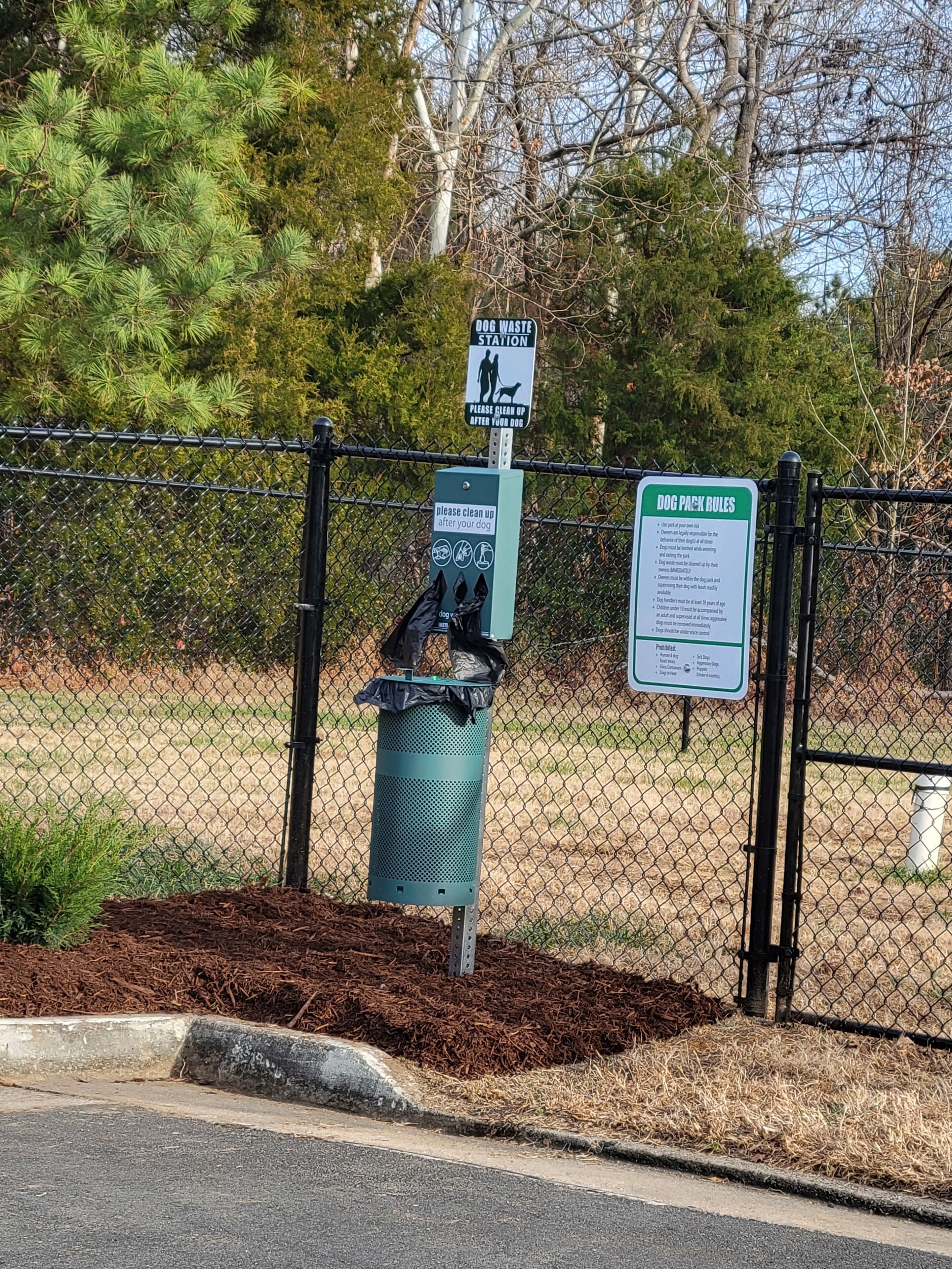 A fenced dog waste station with a trash bin and informational signs.