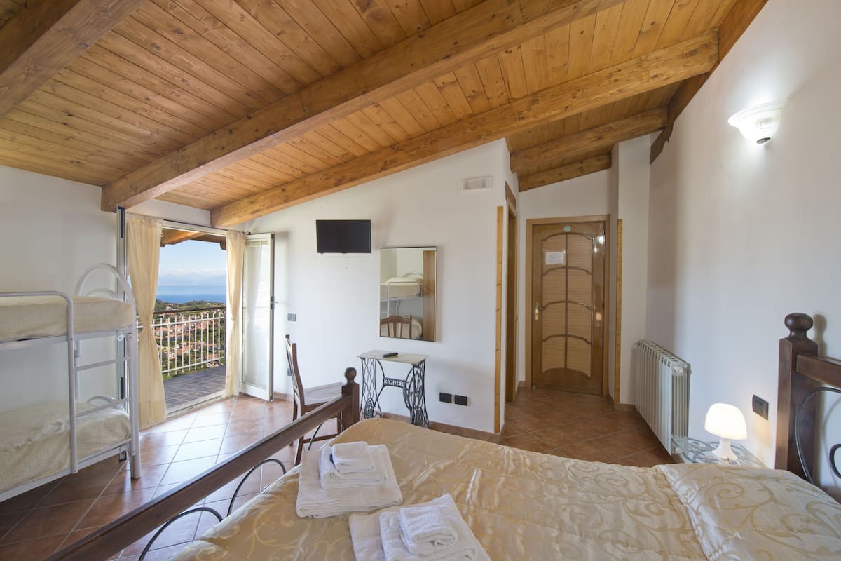 Une chambre avec un plafond en bois, un lit avec des serviettes soigneusement pliées, une petite table avec une chaise, un miroir et une vue sur l’extérieur.