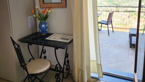 Ein Zimmer mit Tisch, Stuhl, Blumen in einer Vase, einem Spiegel und Blick ins Freie durch ein Fenster.