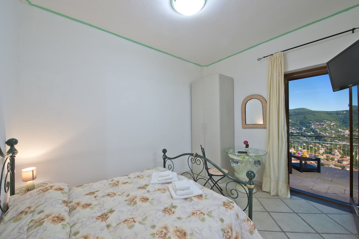 Une chambre à coucher comprenant un lit, une table de chevet, un miroir et donnant sur un balcon avec vue sur la ville.