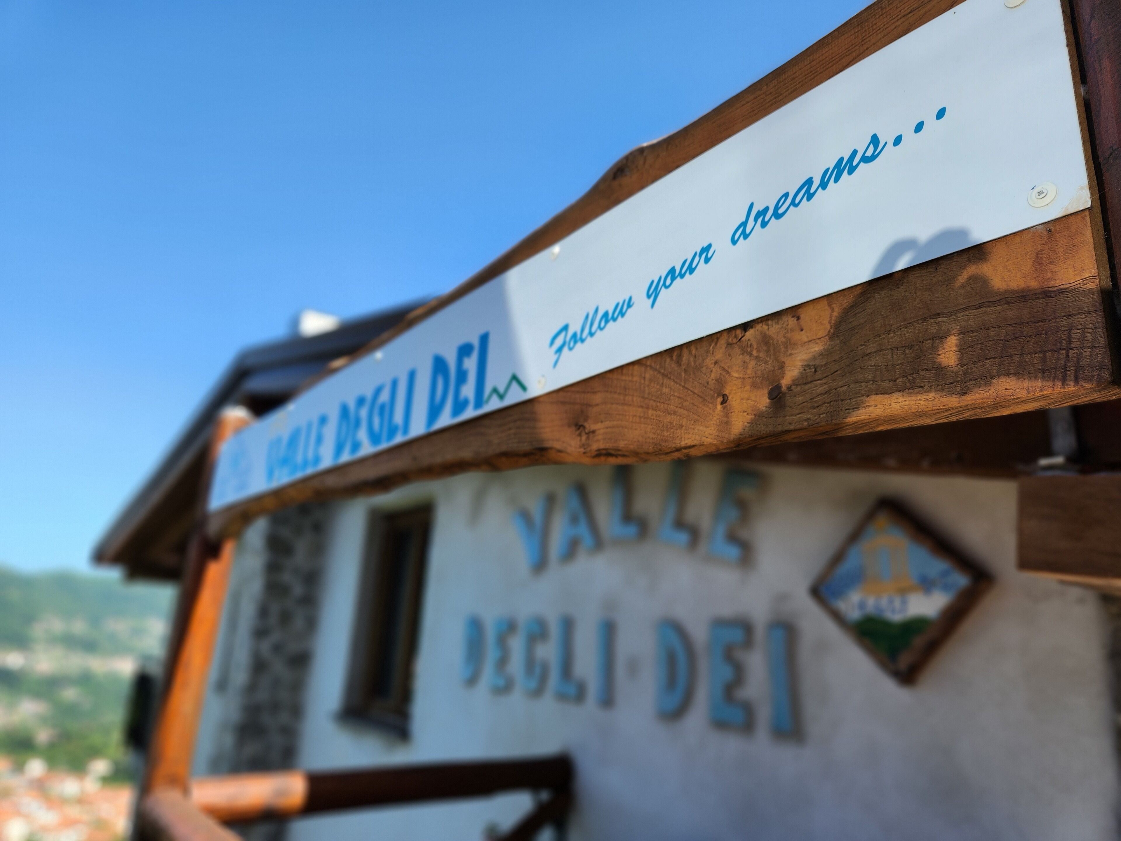 Een bord met 'Valle degli Dei' en 'Volg je dromen...' op een gebouw.