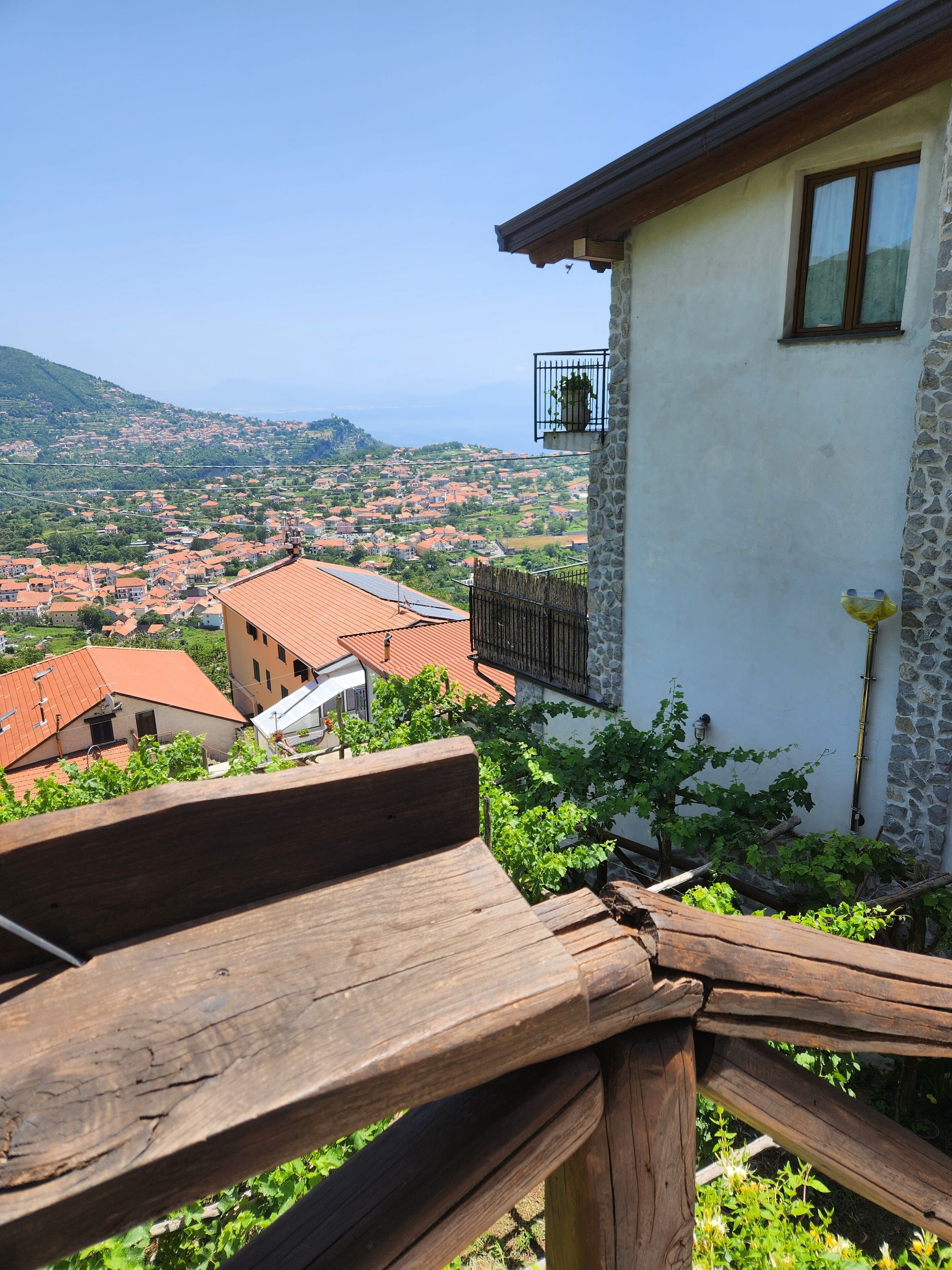 A balcony with a view of a hillside town and the sea.