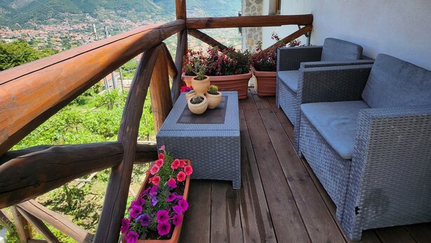 Ein Balkon mit Korbmöbeln, Blumentöpfen und Blick auf eine Stadt und Berge.
