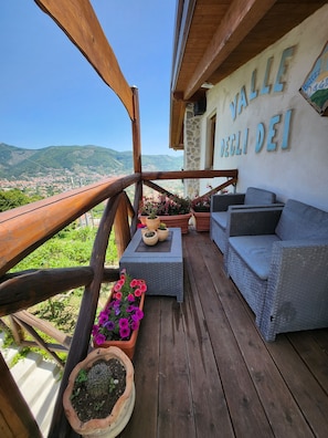 A balcony with wicker furniture, potted plants, and a view of a town and mountains. - Valle degli Dei (Agerola)