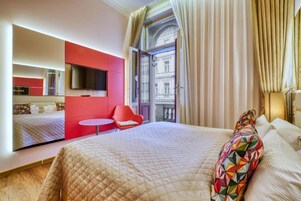 Quarto de hotel com cama grande, parede de destaque vermelha, televisão, mesa redonda pequena e varanda com cortinas.