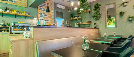 A restaurant interior with booths, tables, hanging plants, and a menu board.