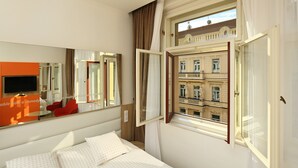 A hotel room with a bed, a TV, a window with curtains, and a view of a building. - Salvator Boutique Hotel (Prague)