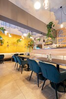 A restaurant interior with a yellow wall, blue chairs, and hanging plants.