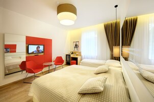 Quarto de hotel com cama, escrivaninha, cadeira e televisão.