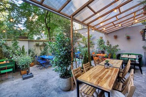 An outdoor patio with wooden tables and chairs, surrounded by potted plants and a glass ceiling structure. - Salvator Boutique Hotel (Prague)