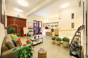 A hotel lobby with a sofa, coffee table, potted plants, a reception desk, and a bookshelf.