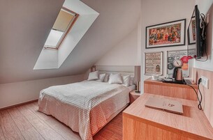 Quarto com teto inclinado, uma cama, uma escrivaninha com um laptop e obras de arte na parede.