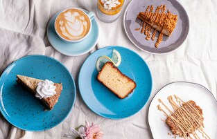 Uma mesa com diversos alimentos, incluindo uma fatia de torta, um pedaço de bolo e uma xícara de café.