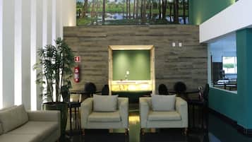 Un hall d’entrée moderne avec un canapé blanc, une table basse avec des magazines, un tableau représentant des palmiers et un mur vert.