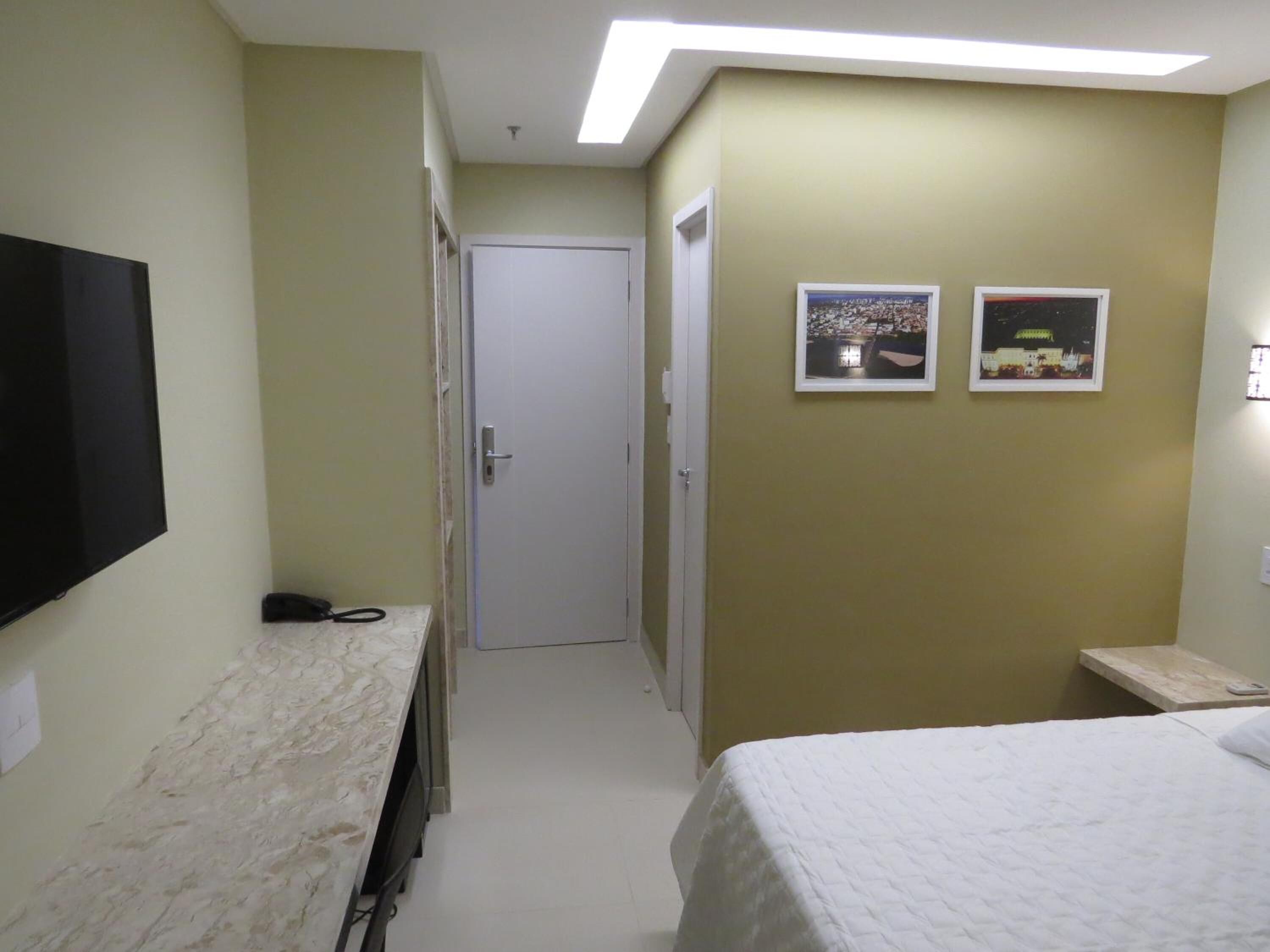 A hotel room with a bed, a desk, a television, and a door leading to a hallway.