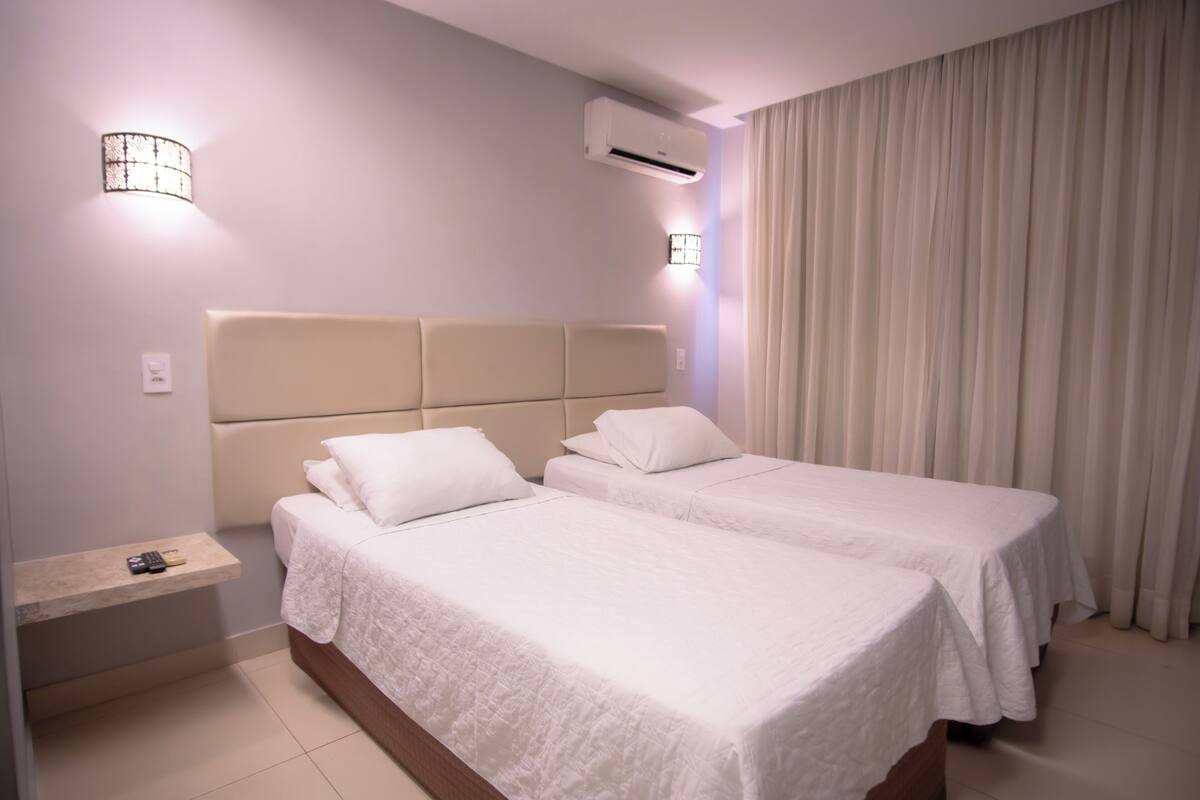 Een hotelkamer met twee bedden, een nachtkastje, een wandairconditioner en een gordijn.