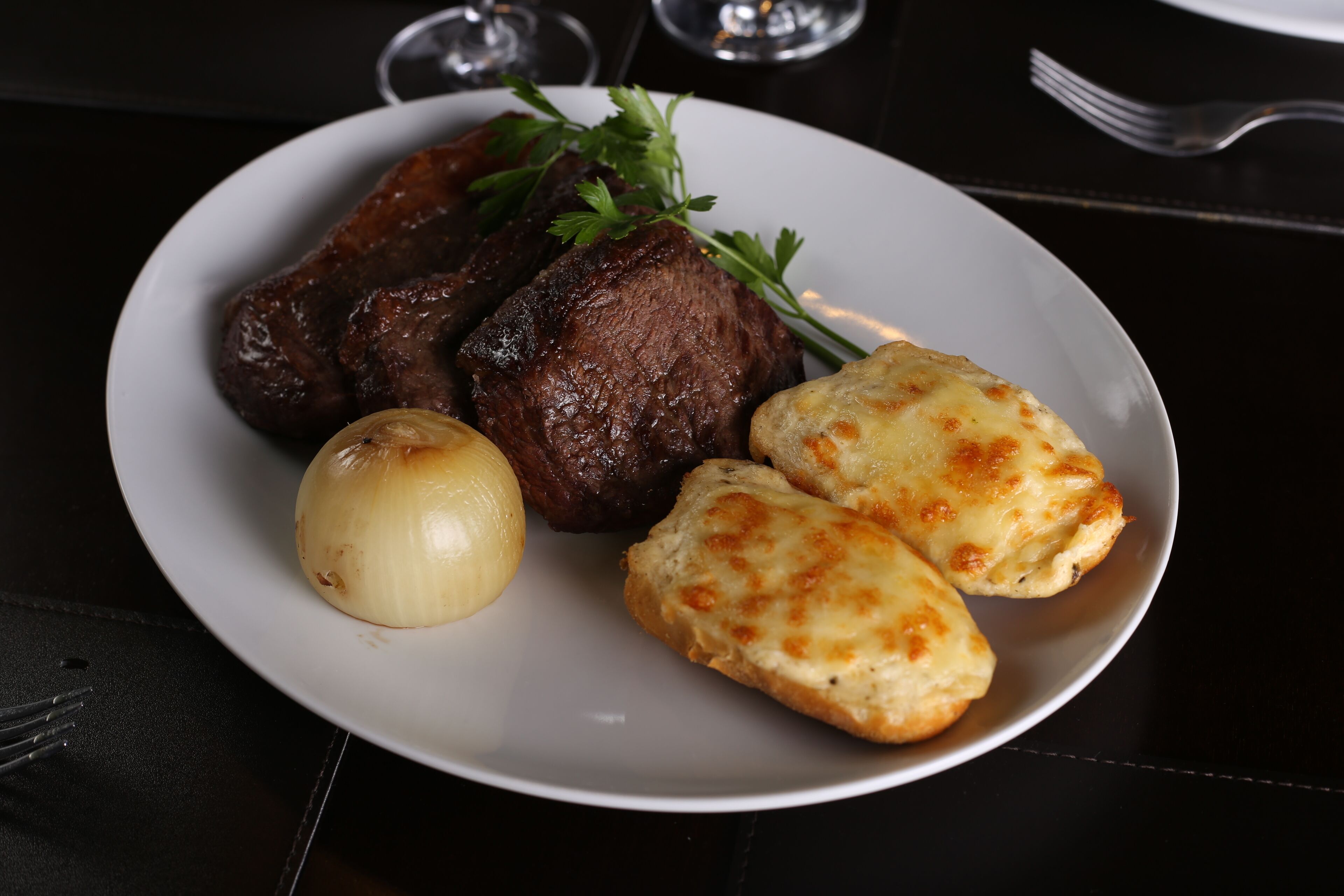 Un plato con carne a la parrilla, una papa hervida y dos rebanadas de pan con ajo.