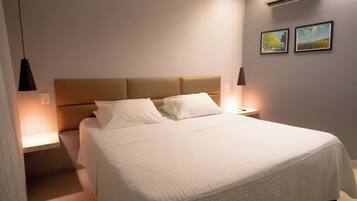 A neatly made bed with a headboard, two bedside tables with lamps, and two framed pictures on the wall.