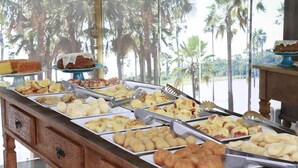 A buffet with various pastries and desserts, arranged on trays with tongs.