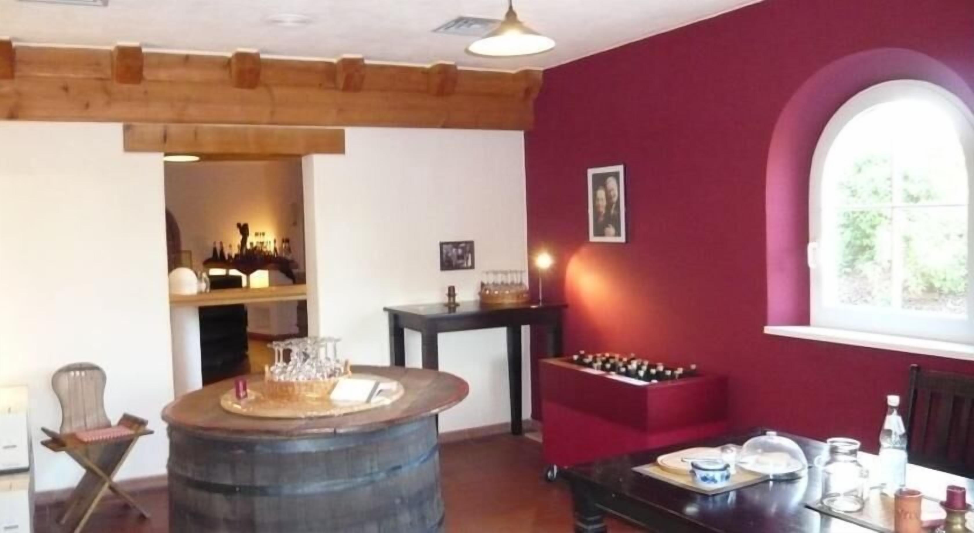 A room with a wooden barrel, a table with glasses, a red wall, and a window.