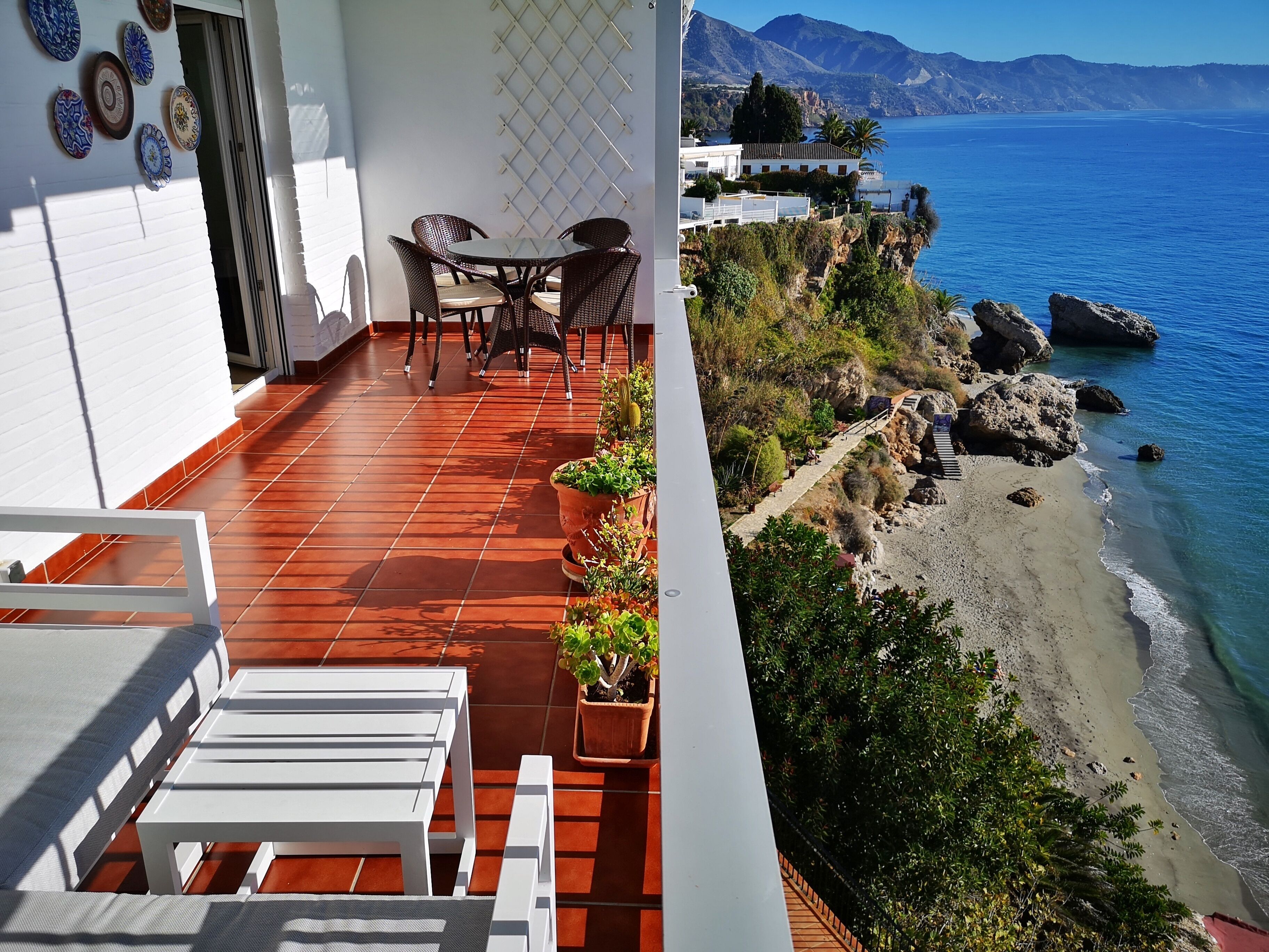A balcony with a tiled floor, a table, chairs, and potted plants.