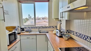 Cocina compacta con lavavajillas, microondas y ventana con vistas a una zona residencial.
