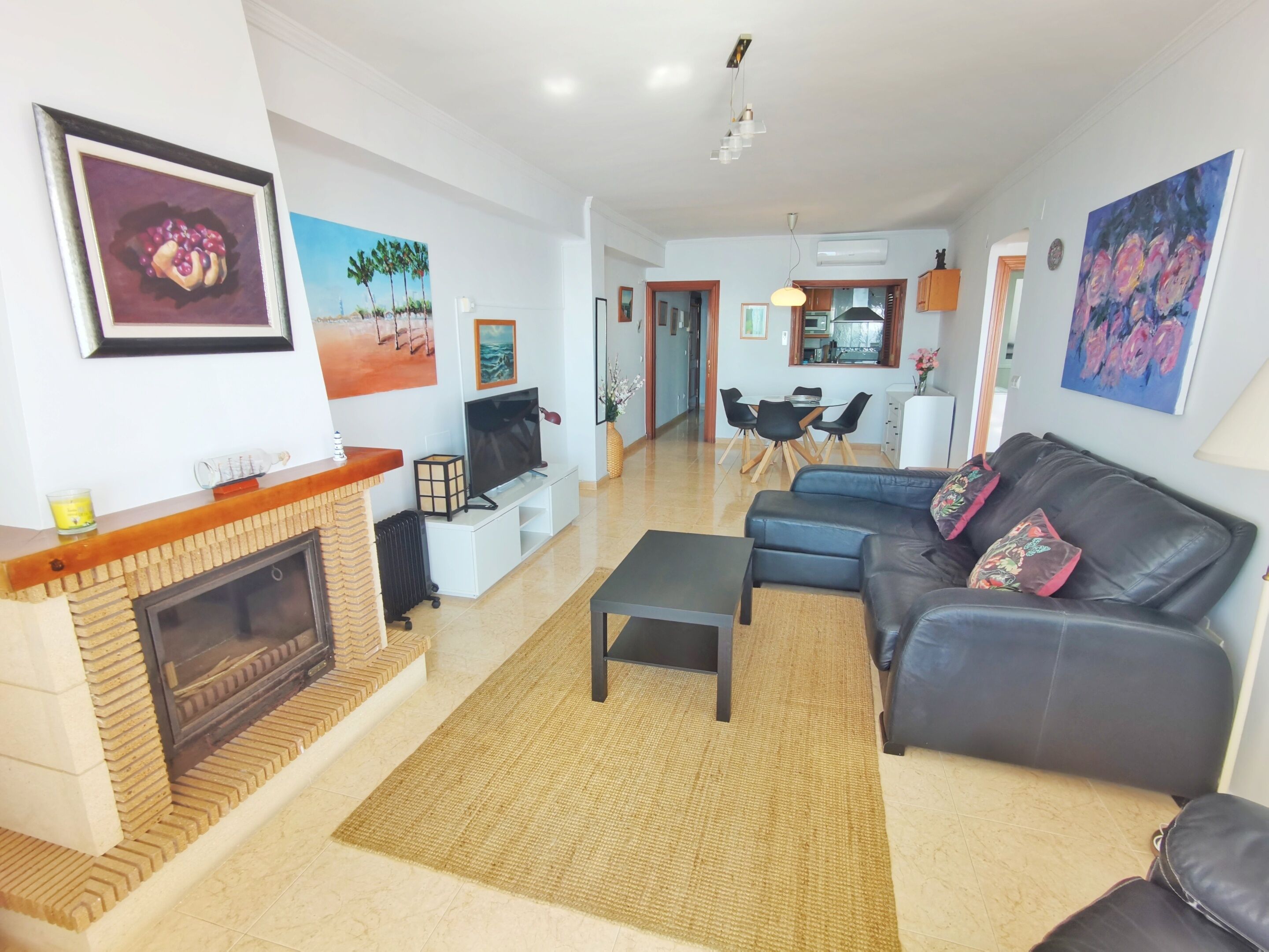 Een woonkamer met een open haard, een bank, een salontafel en een televisie. Er is een eethoek met een tafel en stoelen.